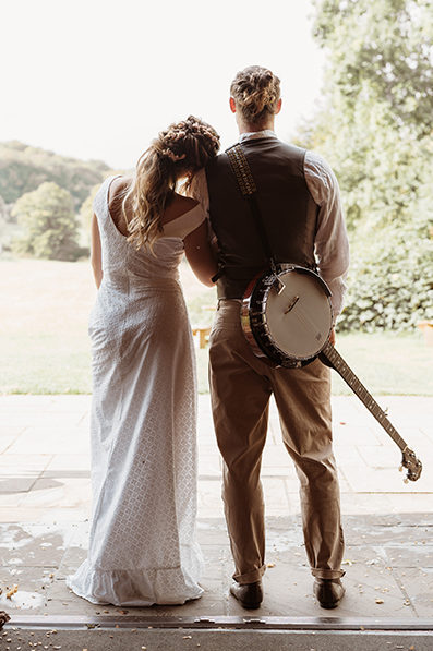bride and groom viewed from the back looking at onto fields. Groom has a banjo