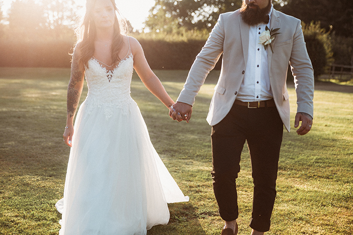 bride and groom walking in a field at sunset