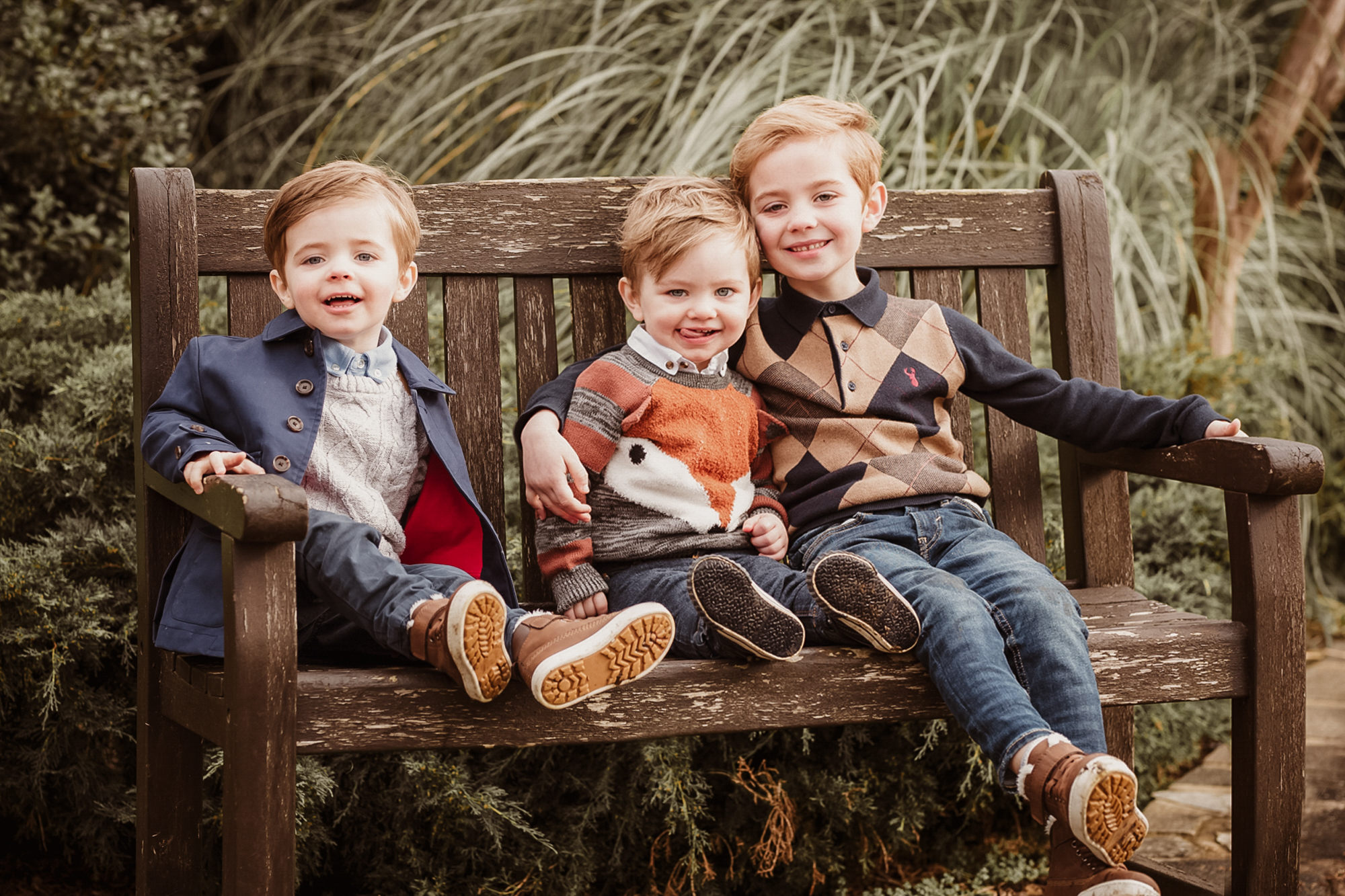 three little brothers sat on bench smiling at camera