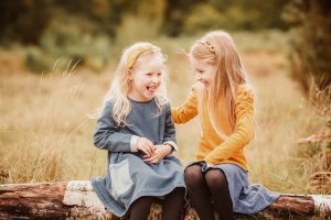 sisters laughing in woods sat on tree trunk