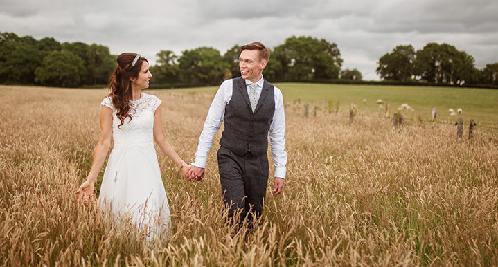 bride and groom walking through wheat field.