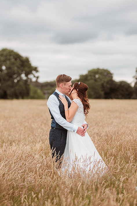bride and groom in wheat field kissing
