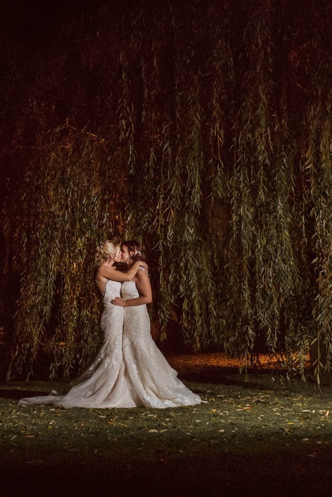 lesbian wedding, two brides at night kissing in front of willow tree