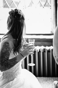 Bride looking out window at Cain Manor with glass of prosecco. B&W