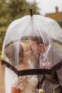 Bride and groom kissing under a clear umbrella.