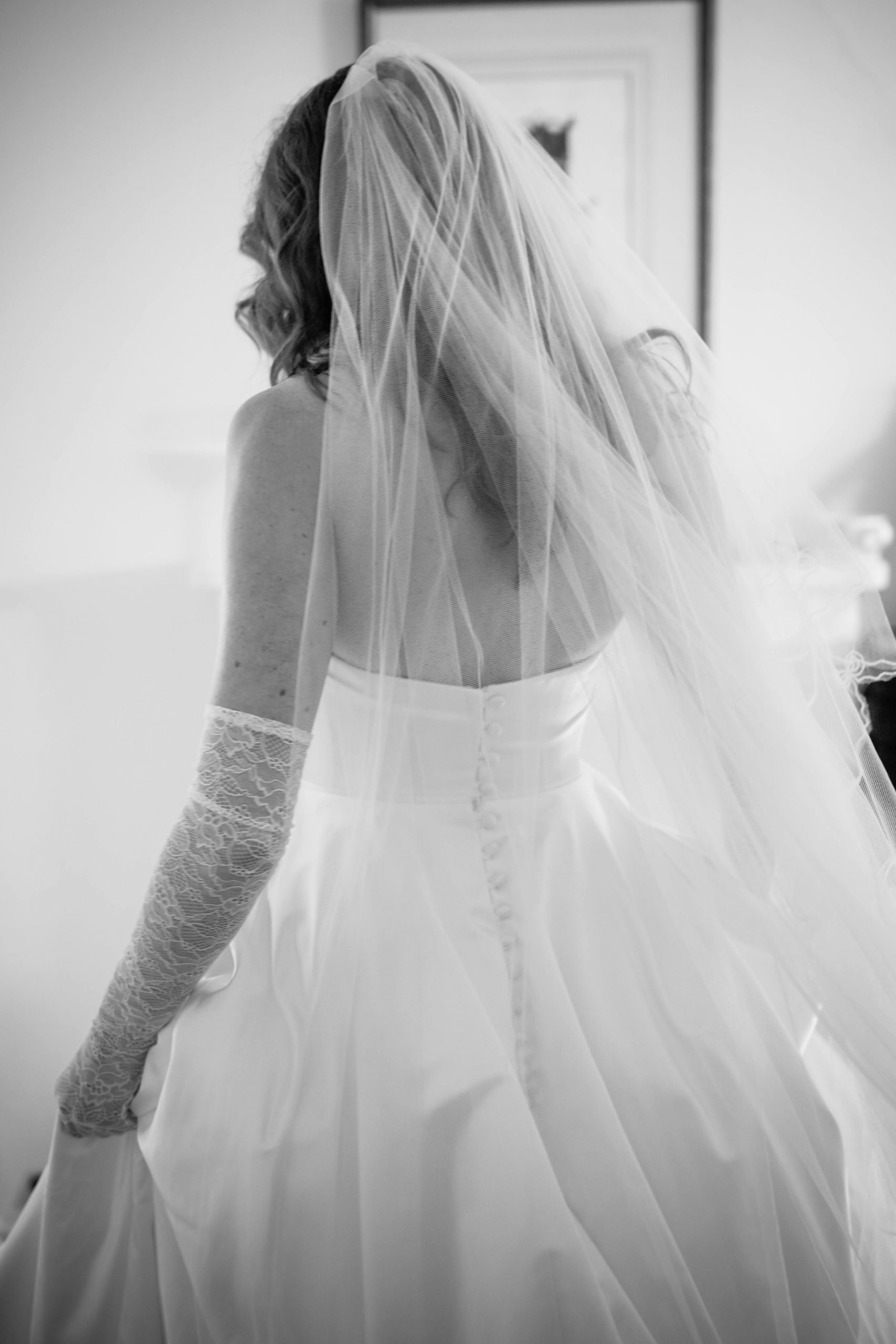 Bride with back to camera. She wears a veil and gloves. Photo is B&W